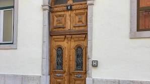 A double wooden door with a number '6' above it, set in a building with a stone base and a tiled ground.
