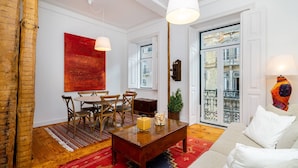 A living room with a wooden coffee table, a red rug, a white sofa, and a dining area with chairs and a table.