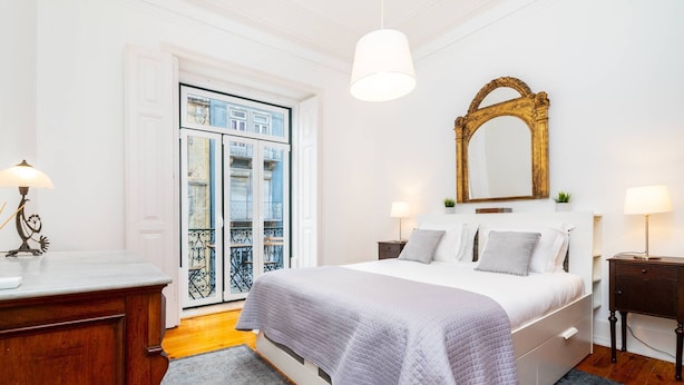 A bedroom with a large bed, bedside tables, a mirror, and a door leading to a balcony.