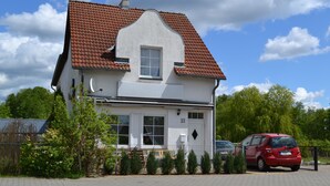 Une maison à deux étages, avec un toit recouvert de tuiles rouges, une façade blanche et le numéro 21 sur la porte.