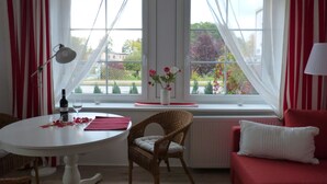 Une pièce comprenant une table à manger, une chaise en osier, un canapé rouge et une fenêtre avec des rideaux.