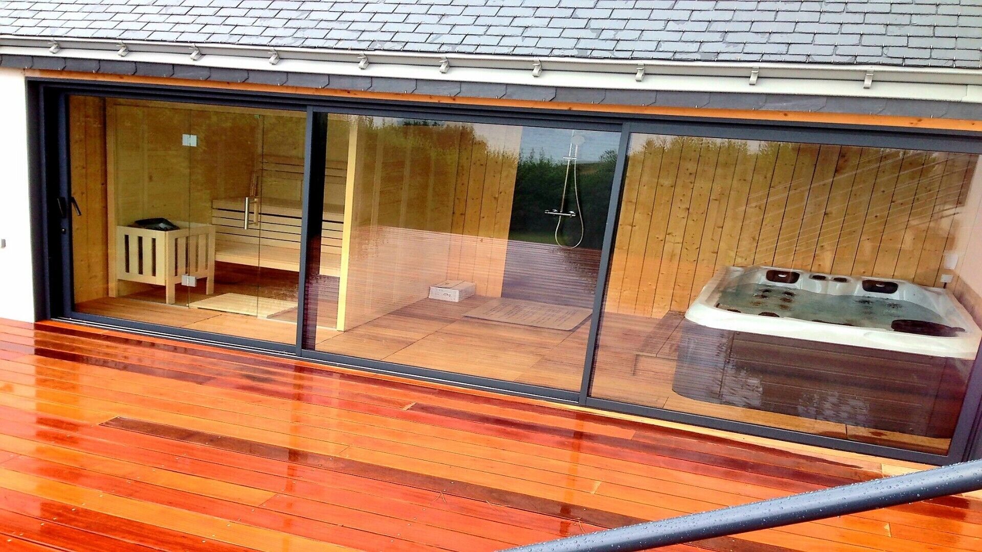 A modern house with a large sliding glass door leading to a wooden deck and a hot tub.
