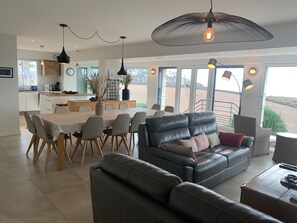 Een moderne woonkamer met een leren bank, een eettafel en stoelen. Er is een keuken met een raam en een eettafel.