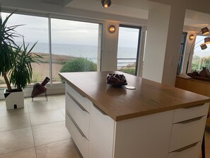Een moderne keuken met een ruim kookeiland, witte kasten en uitzicht op de oceaan.