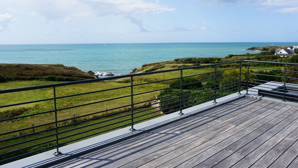 A wooden deck with a metal railing overlooking a coastal landscape with grassy areas and a view of the sea. - Villa FEUNTEUN on the ocean! (Clohars-Carnoët)