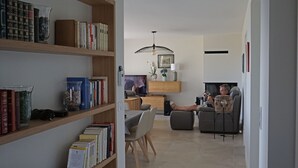 A modern living room with a bookshelf, a dining area, and a seating area with a fireplace. - Villa FEUNTEUN on the ocean! (Clohars-Carnoët)
