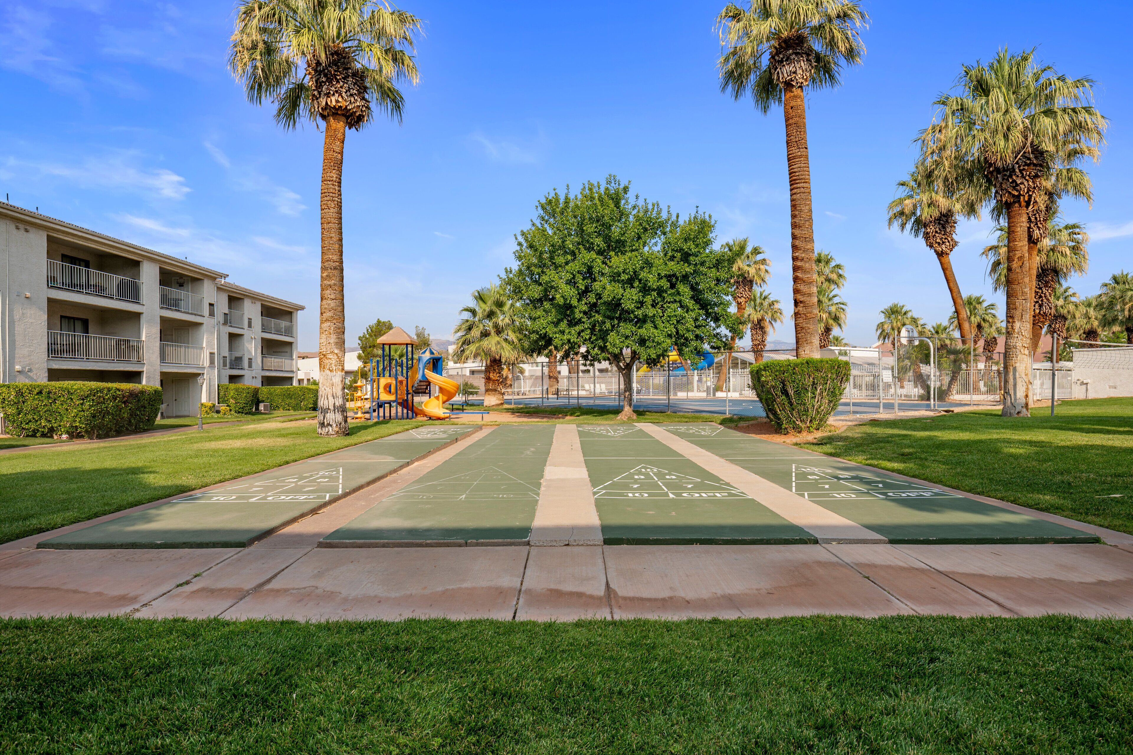 A courtyard with a shuffleboard court, palm trees, and a playground.