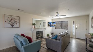 A living room with a fireplace, a ceiling fan, and a television. - Las Palmas Resort 704, Newly Renovated Main level 3 bd unit, Close to pool + More (St. George)