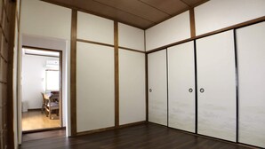 A room with a wooden floor, sliding doors, and a visible kitchen area with a dining table and chairs. - Not Ninja Osaka Hirano 1 (Osaka)