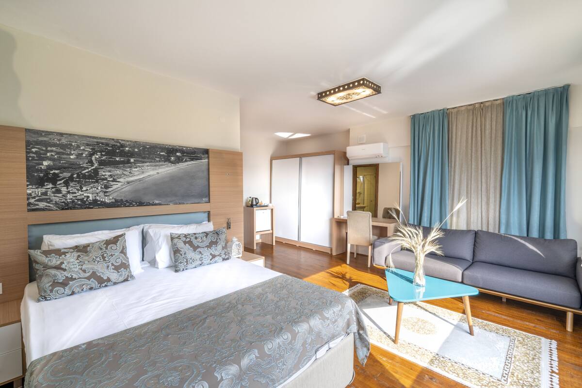 Habitación de hotel moderna con una cama grande, un sofá, un escritorio y vistas a un paisaje urbano.