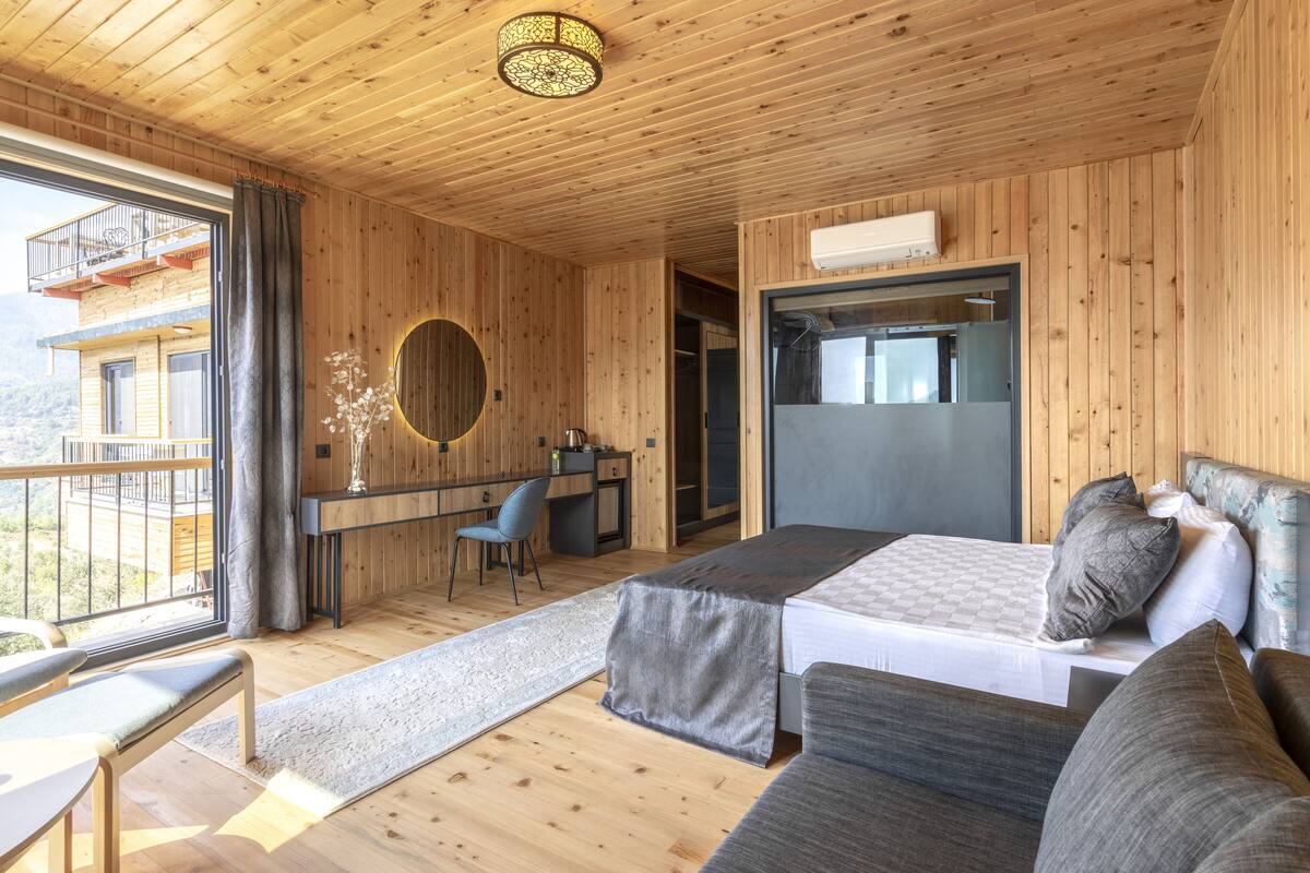 Habitación tipo cabaña de madera con cama, escritorio y vista a un balcón.