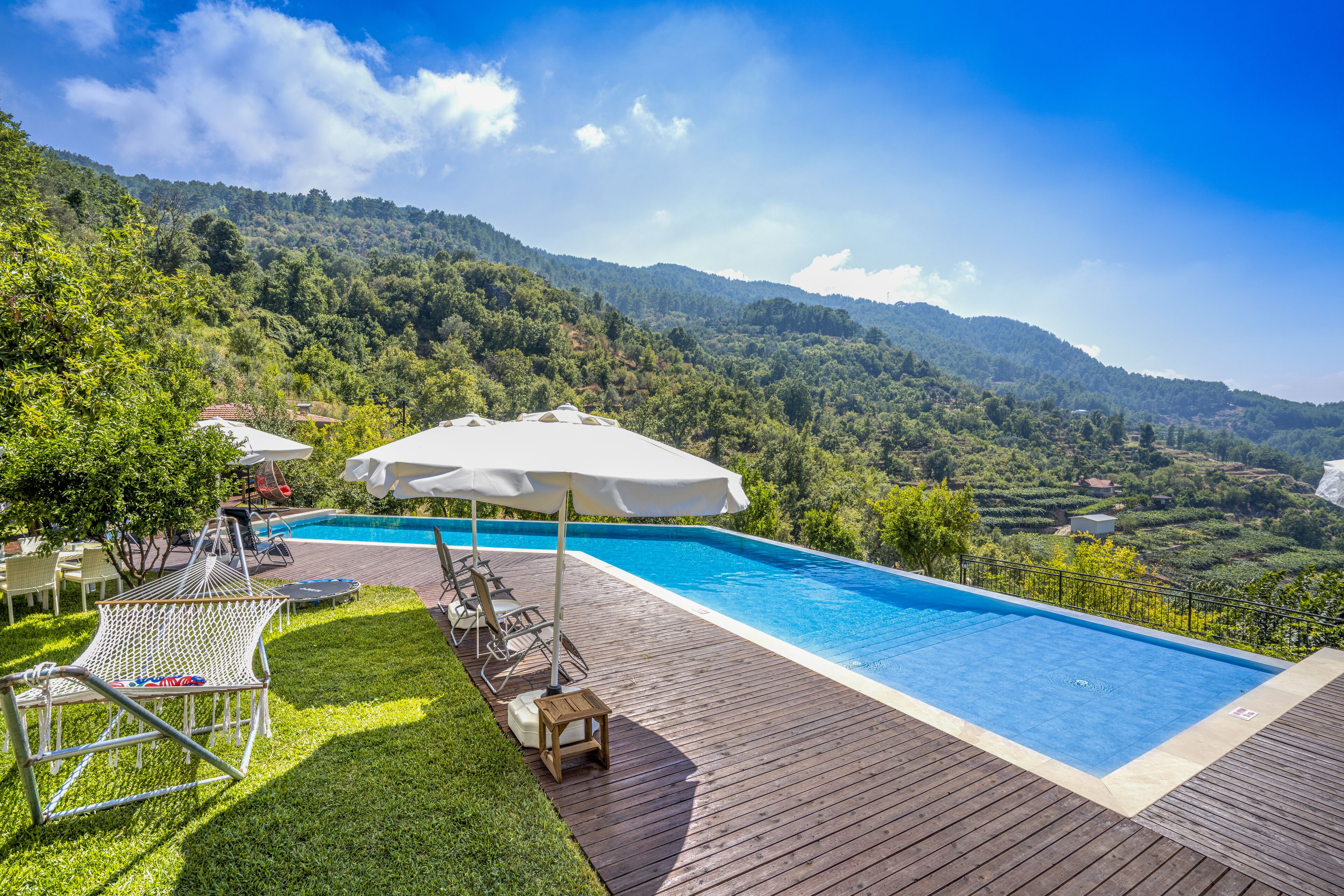 Piscina com deck de madeira, espreguiçadeiras e guarda-sóis.