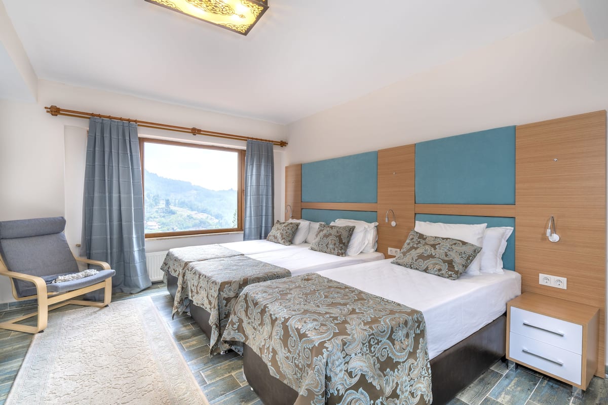 Habitación de hotel con dos camas, una silla, una mesita de noche y una ventana con cortinas.