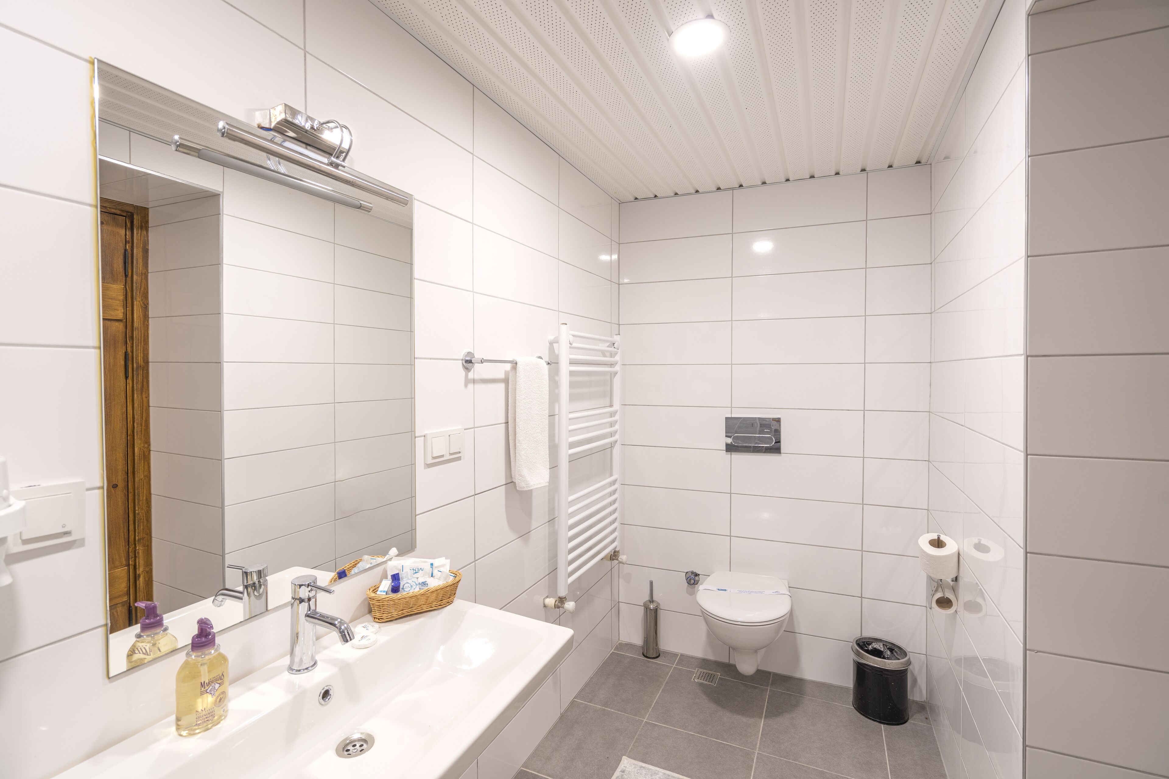 Une salle de bain moderne avec un grand miroir, des carreaux blancs, une baignoire, des toilettes et une poubelle.