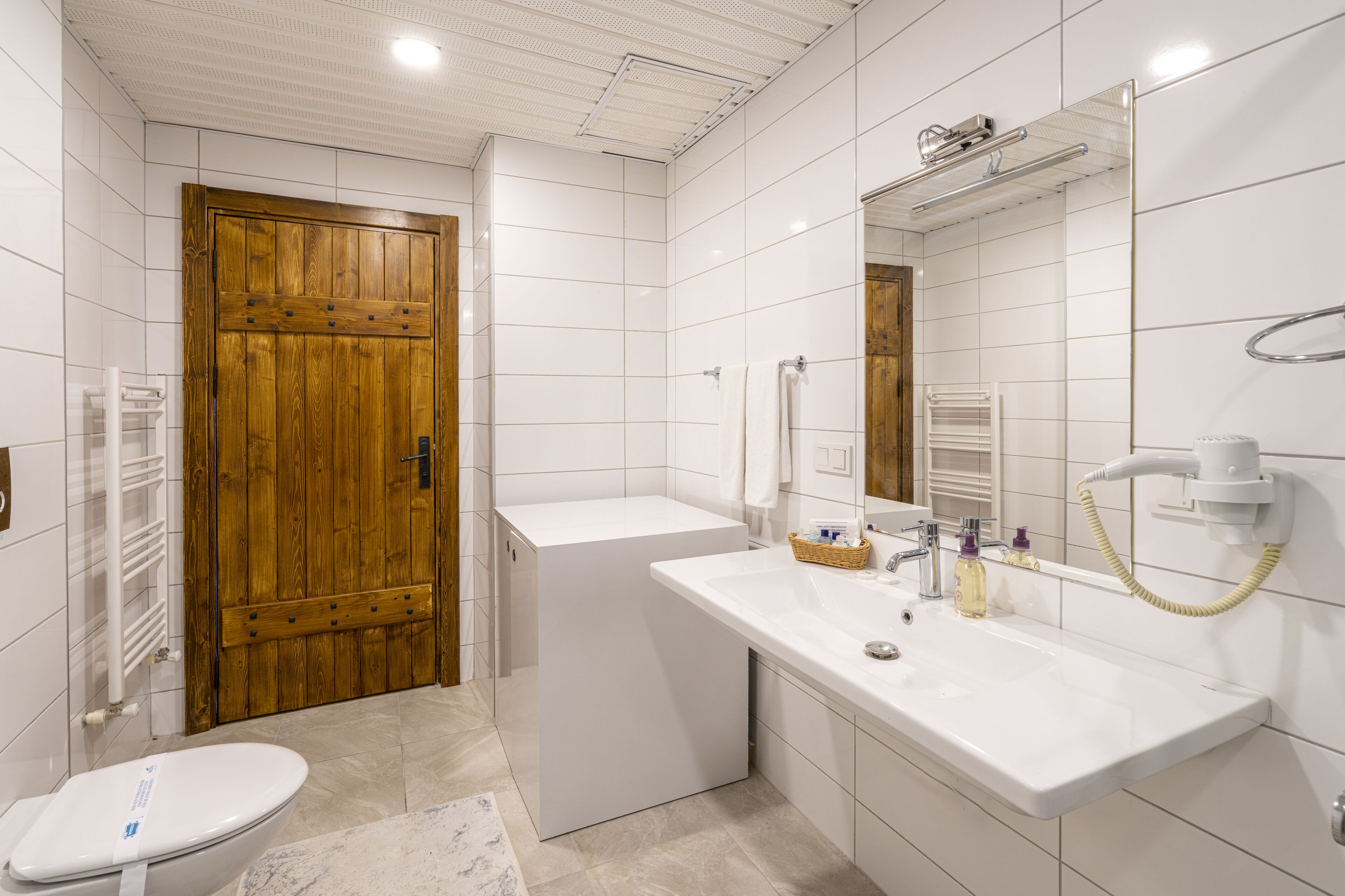 Un baño moderno con una puerta de madera, un lavabo blanco y un espejo grande.