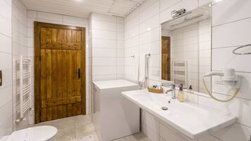 Un baño moderno con una puerta de madera, un lavabo blanco y un espejo grande.