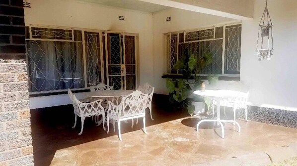 Un patio con dos mesas y sillas blancas, una planta en maceta y un lámpara colgante.