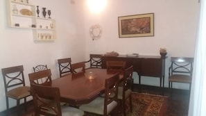 Zona pranzo con tavolo e sedie in legno, un ripiano con bicchieri, un quadro appeso al muro e un tappeto sul pavimento.