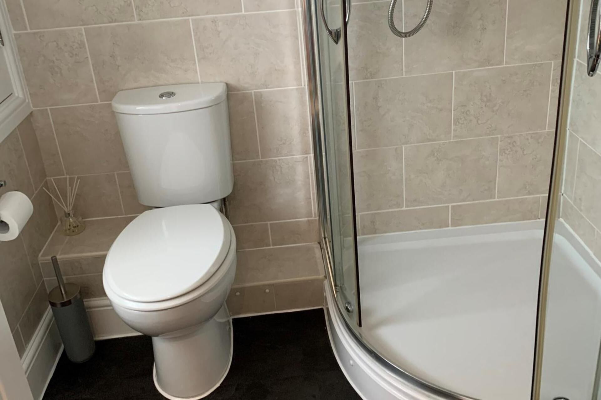 A bathroom with a toilet, a glass shower enclosure, and a toilet paper holder.