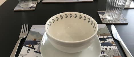 A dining table set with a white bowl, a fork, a knife, and a glass on a placemat with a nautical theme.
