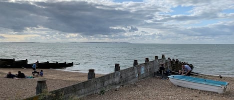 A beach with a wooden pier, people relaxing, and a boat.