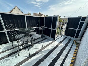 A patio with a table and chairs, a tiled floor with black and white stripes, and a view of houses in the background.