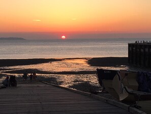 A wooden pier extending into a calm sea at sunset with a boat named 'KIKI' docked at the end.