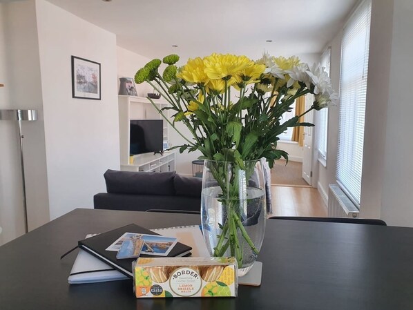 Et spisebord med en vase gule blomster, en notesbog og en kasse citronmåne kage.