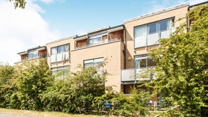 Un moderno edificio de apartamentos con varios balcones, fachada de ladrillo y vegetación circundante.