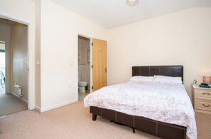 A bedroom with a bed, a nightstand, and a door leading to a bathroom. - Rustat Gold (Cambridge)