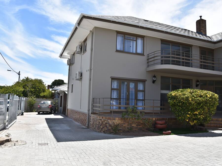A two-story residential building with a balcony, a garage, and a well-maintained garden.