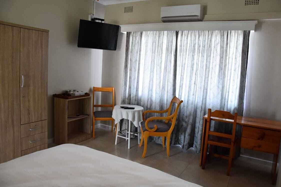 A hotel room with a bed, a TV mounted on the wall, a desk, two chairs, and a window with curtains.