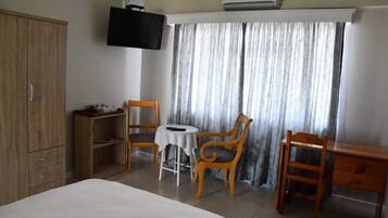 A hotel room with a bed, a TV mounted on the wall, a desk, two chairs, and a window with curtains.