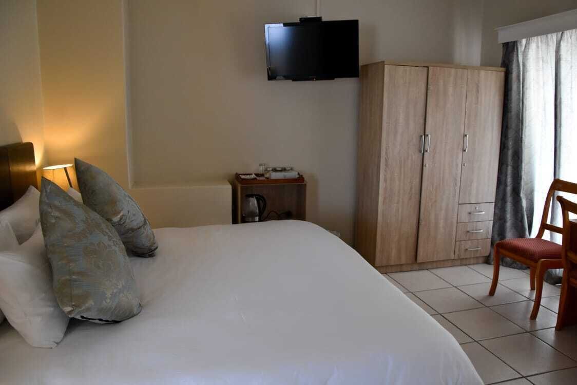Un dormitorio con cama, almohadas, televisor montado en la pared, armario, silla y una mesita con tetera.