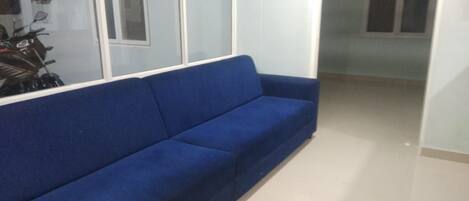 Un sofá azul en una habitación con suelo de baldosas y una ventana.