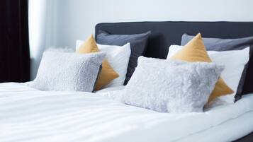 A neatly made bed with white linens and multiple pillows in shades of gray and mustard.