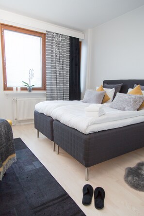 Une chambre à coucher moderne avec un grand lit, une fenêtre avec des stores, un radiateur et une petite plante posée sur le rebord de la fenêtre.