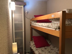 A bunk bed with floral bedding and red pillows, a wall-mounted heater, and a door with a frosted glass panel. - Studio at the foot of the slopes in Corrençon (Corrençon-en-Vercors)