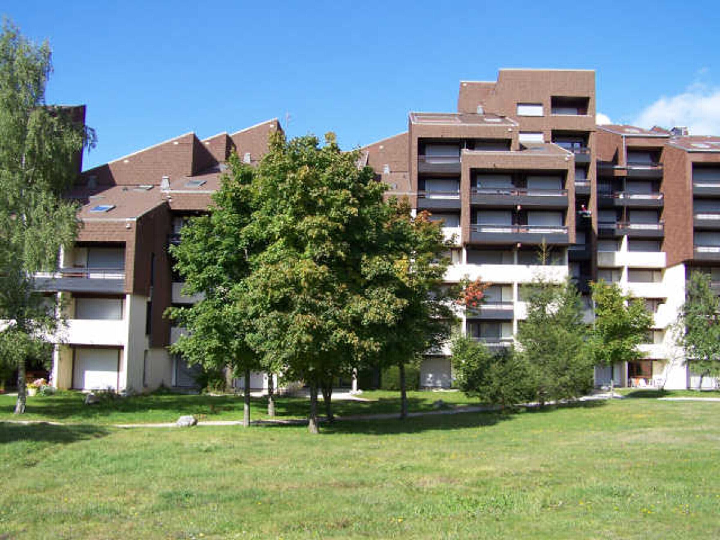 Un edificio residencial de varios pisos con balcones, rodeado de césped y árboles.