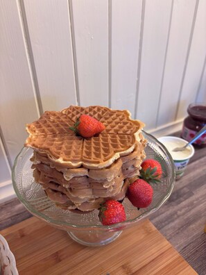 A stack of waffles with strawberries on a glass plate.