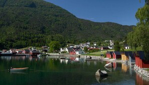 A coastal village with houses and boats on calm water, surrounded by forested hills.