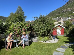 Two people seated at a table in a garden with a red shed and a house in the background.