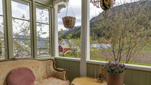 A room with a sofa, a small table, and a view of a mountain landscape through large windows.