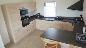 A modern kitchen with light wood cabinets, a black countertop, stainless steel appliances, and a window providing natural light. - Ty Bihan, the "Little house" exceptional sea view! (Doëlan Clohars-Carnoët)