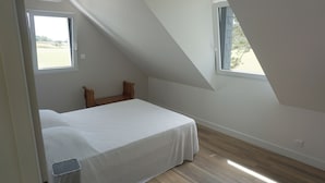 A bedroom with a sloped ceiling, a bed with a white bedspread, two windows, and a view of the outdoors. - Ty Bihan, the "Little house" exceptional sea view! (Doëlan Clohars-Carnoët)