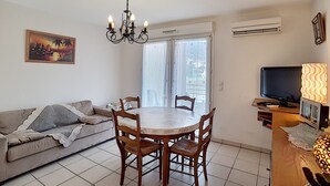 Een woonkamer met een bank, eettafel, stoelen, een kroonluchter, een televisie en een airconditioner.