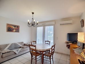 Una sala de estar con sofá, mesa de comedor, sillas, candelabro, televisor y aire acondicionado.