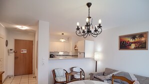 Een eethoek met een ronde tafel, stoelen en een kroonluchter. In de achtergrond bevindt zich een keuken met een koelkast en een magnetron.