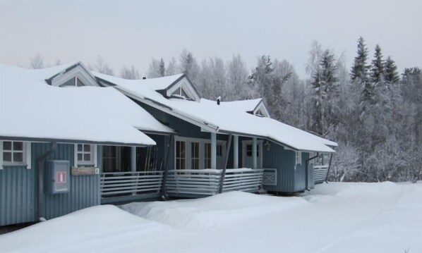 A snow-covered building with a porch and a stack of firewood.