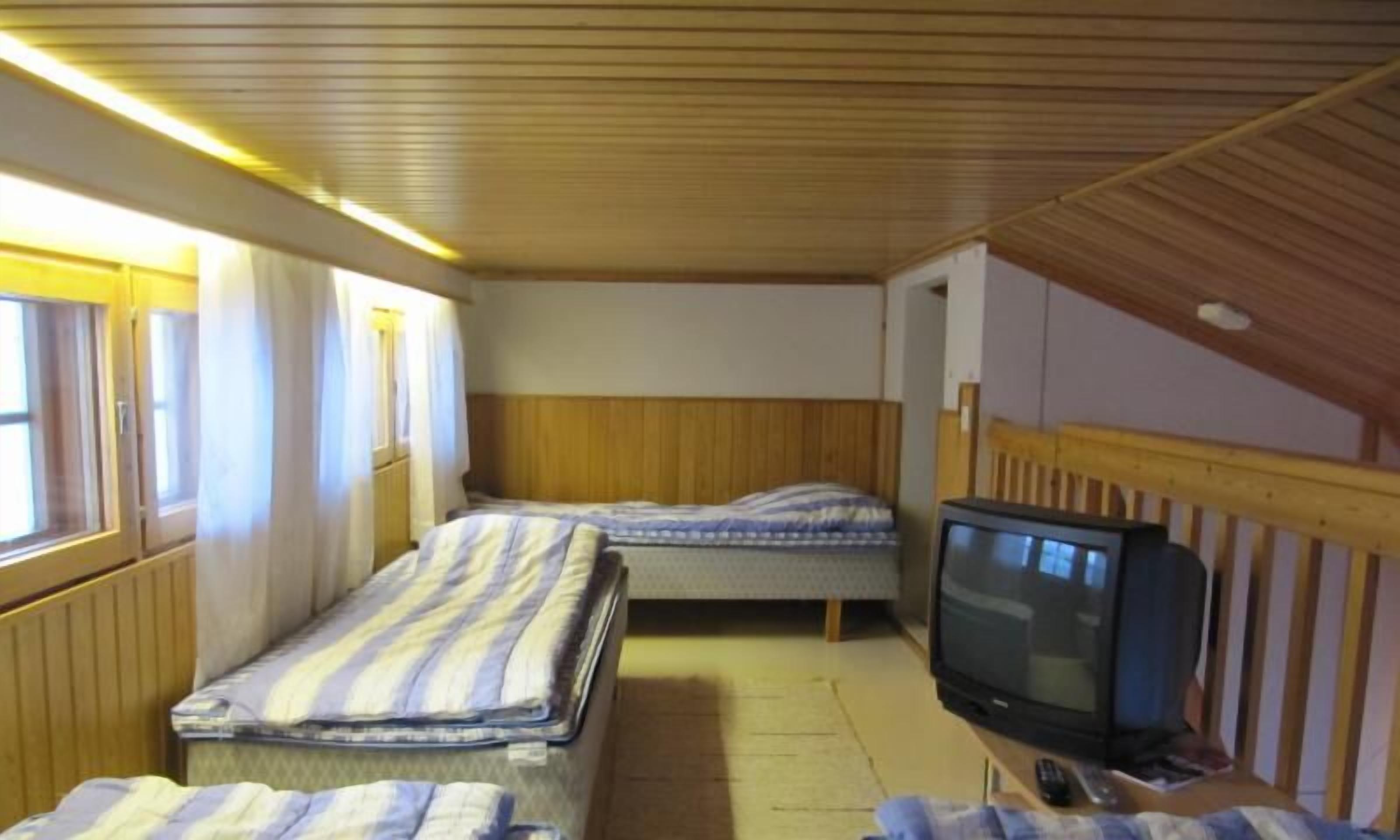 Ett litet rum med två sängar, en tv och ett fönster.